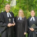 Zwei Frauen und ein Mann im Talar lächeln in die Kamera
