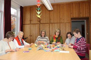 Sechs Frauen am Tisch basteln Faltkraniche.