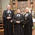Ein Mann und zwei Frauen in geistlicher Kleidung stehen vor einem Altar und lächeln in die Kamera