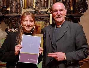 Ein Mann und eine jüngere Frau stehen zusammen vor einem Altar. Die Frau hat eine Urkunde in der Hand.
