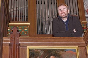 Ein Mann steht lächelnd vor einer Orgel
